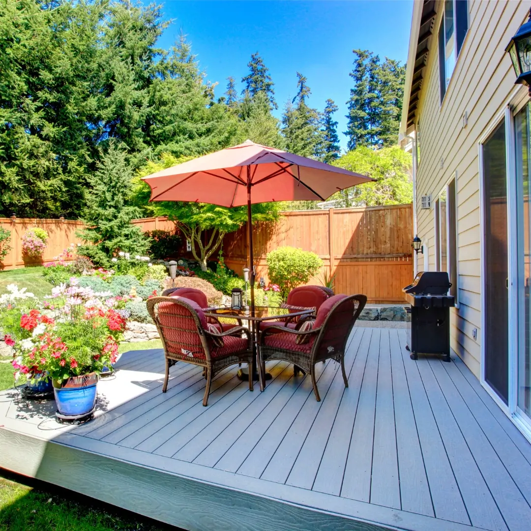 Backyard deck with patio furniture, umbrella and grill beside a Westchester County home