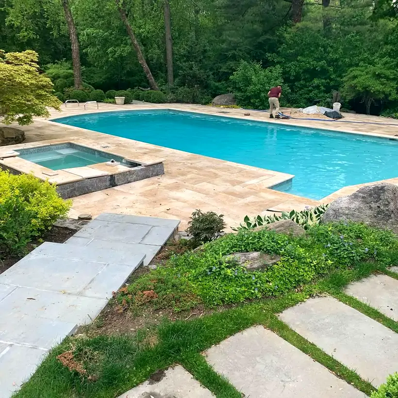Travertine pool deck and spa surround with a bluestone stepping-stone path, built by Angel’s Pools in Westchester County