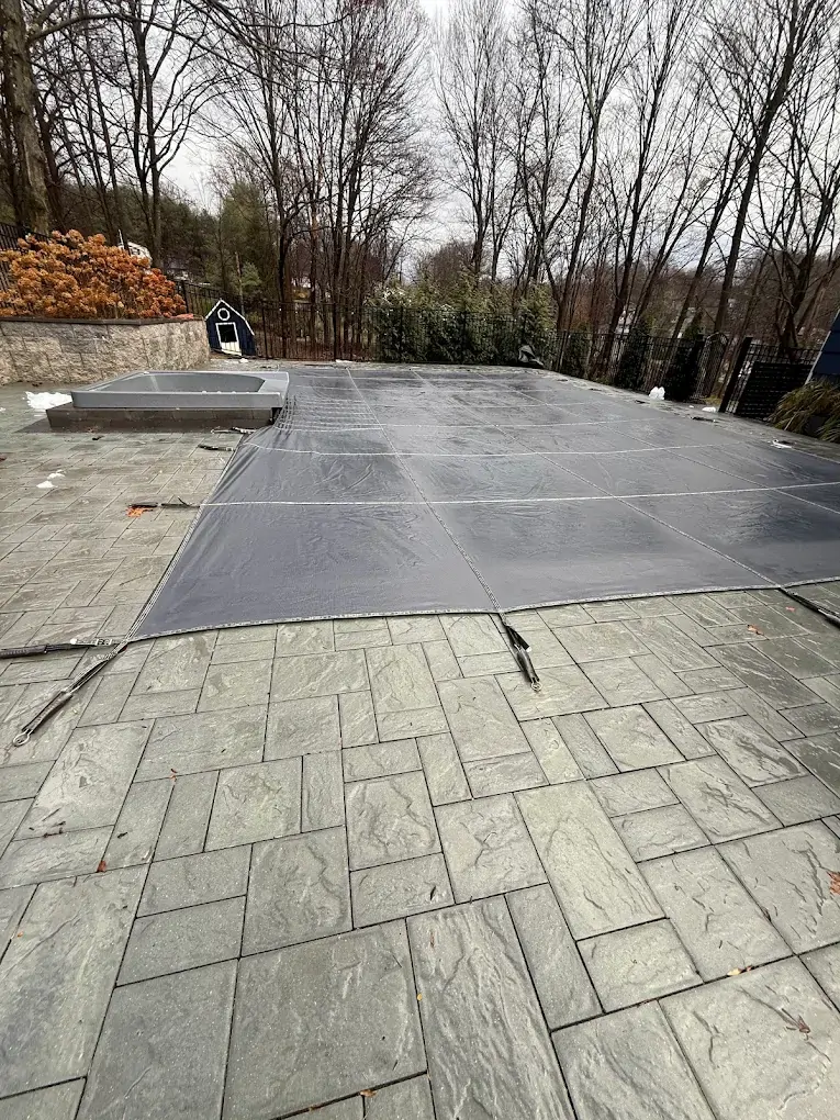 Mesh safety cover fitted over an inground pool on a bluestone patio for winter closing
